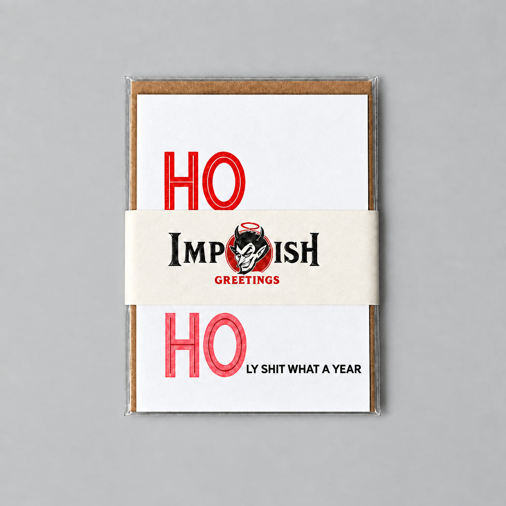 A stack of greeting cards from Impish Greetings featuring a bold red and black holiday design, wrapped in a beige paper band, placed on a textured gray concrete surface.