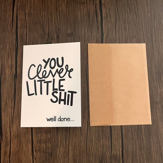 Impish Greetings Clever Little Shit congratulations card with black typography on white cardstock and kraft envelope.