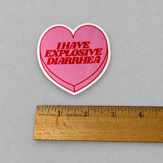 Impish Greetings heart-shaped pink vinyl sticker with red text reading I HAVE EXPLOSIVE DIARRHEA next to a ruler.