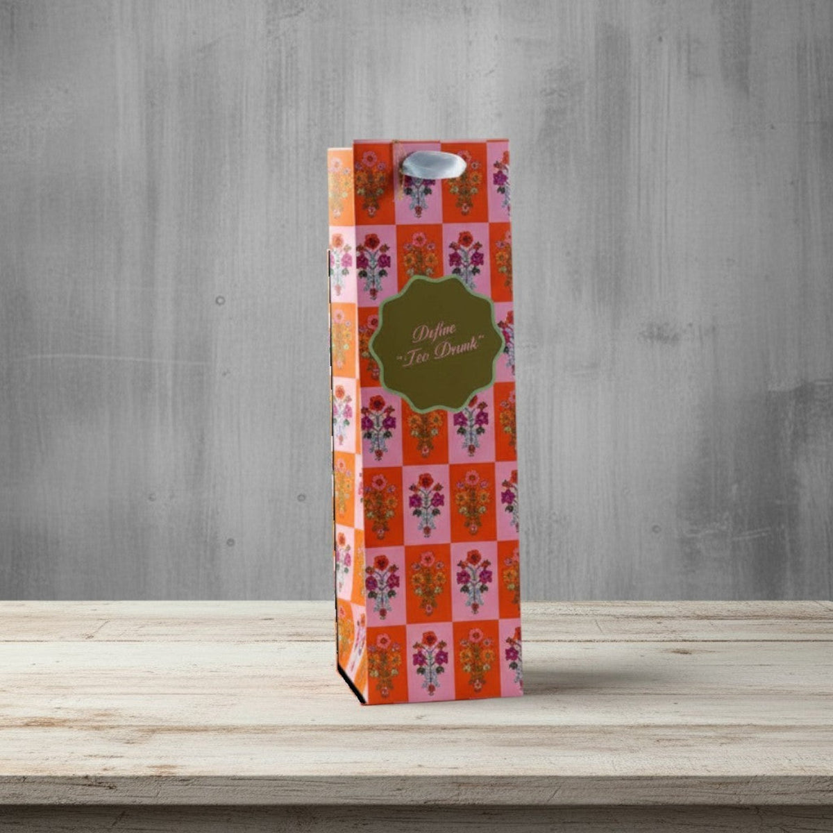 Impish Greetings floral wine bag with Too Drunk text, metallic ribbon handles, and a gift tag on a wooden table.