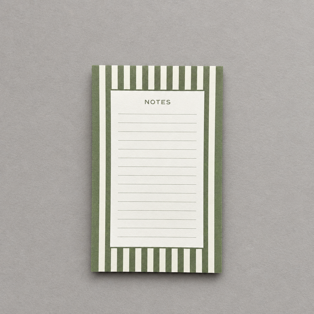Impish Greetings green and white striped notepad with lined pages for notes on a neutral grey background.