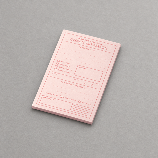 Impish Greetings Grown-ass Person memo pad with pink paper and red ink on a grey background.