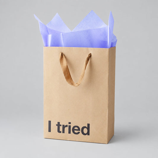 Impish Greetings kraft paper gift bag with I tried text and purple tissue paper on a light grey background