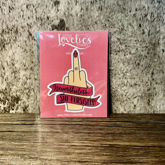 Impish Greetings Nevertheless She Persisted vinyl sticker featuring a hand with a middle finger gesture on pink card