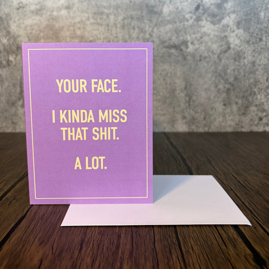 I Miss Your Face purple greeting card with yellow text and a white envelope on a wooden table.