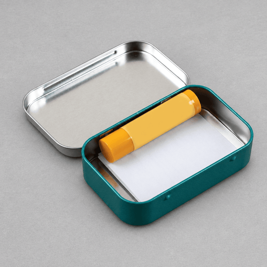 Impish Greetings Very Important Shit Stash Tin, a teal metal hinged container holding a yellow lip balm and paper.