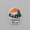 A die-cut sticker featuring a retro-style illustration of a mama bear and cub under a striped sunset, with the words 'Mama Bear' below, shown on a textured gray background.