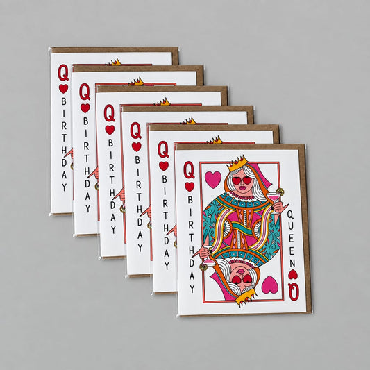A fan of birthday queen playing cards arranged on a textured gray concrete surface. The cards feature a colorful illustration of a crowned queen with sunglasses and a skull design, with 'Q BIRTHDAY' printed vertically on the sides.