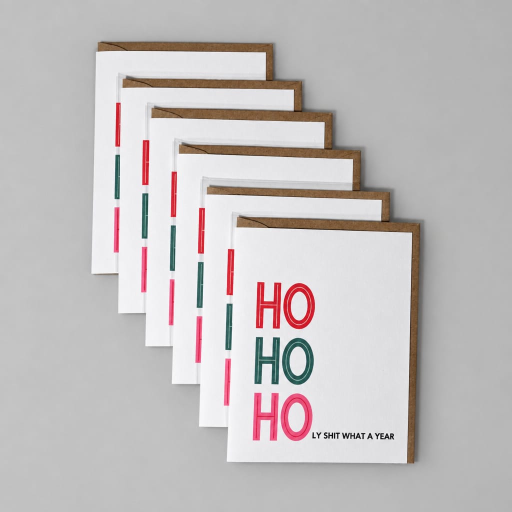 Five stacked white greeting cards with brown edges, featuring the text 'HO HO HO' in red and green, and the phrase 'LY SHT WHAT A YEAR' on a textured gray background.