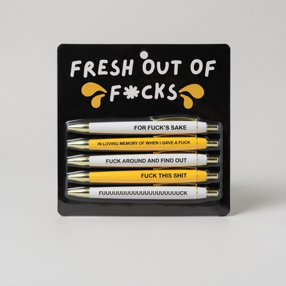 Close-up of white and yellow Fresh Out of Fucks pens on muted light grey background