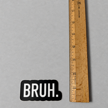 Impish Greetings Bruh vinyl sticker with white text on a black background next to a wooden ruler for scale