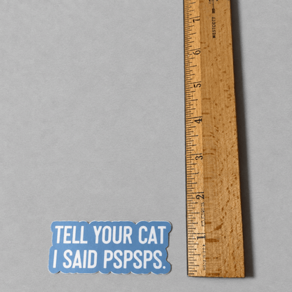 Impish Greetings vinyl sticker with white text Tell Your Cat I Said Pspsps on a blue background next to a ruler.