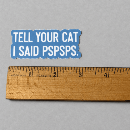 Impish Greetings vinyl sticker with blue background and white text reading Tell Your Cat I Said Pspsps next to a ruler
