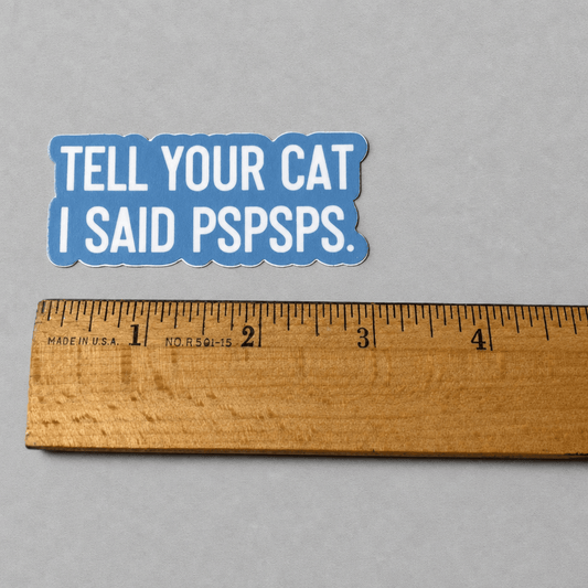 Impish Greetings vinyl sticker with blue background and white text reading Tell Your Cat I Said Pspsps next to a ruler