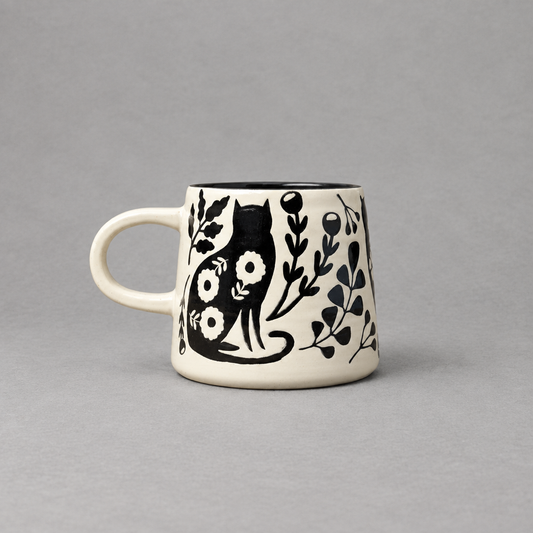 Impish Greetings Catbloom stoneware mug featuring a black cat and floral imprint on a cream background.
