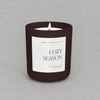 Impish Greetings 15 oz Cozy Season candle in a matte dark brown jar with a white label on a grey background