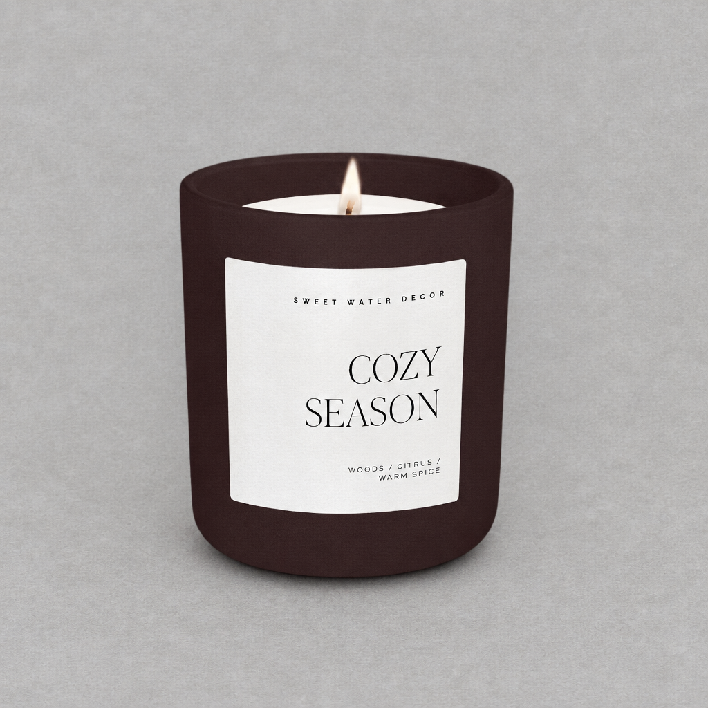 Impish Greetings 15 oz Cozy Season candle in a matte dark brown jar with a white label on a grey background