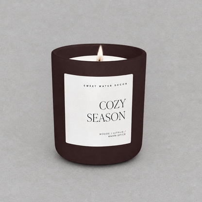 Impish Greetings 15 oz Cozy Season candle in a matte dark brown jar with a white label on a grey background