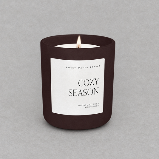 Impish Greetings 15 oz Cozy Season candle in a matte dark brown jar with a white label on a grey background