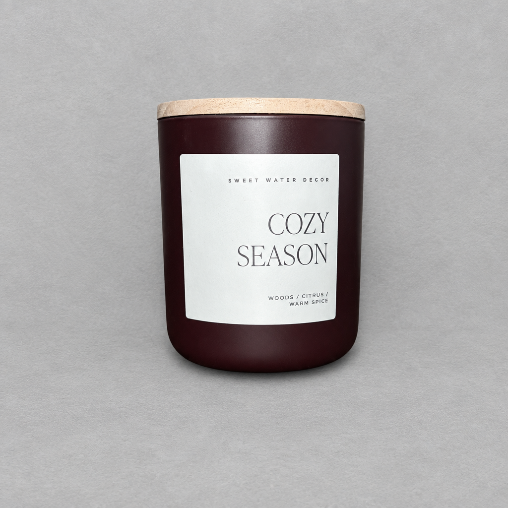 Impish Greetings Cozy Season 15 oz candle in a dark brown matte jar with a wooden lid and minimalist white label
