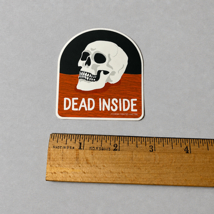 Impish Greetings Dead Inside sticker featuring a white skull on a black and orange background with a wooden ruler