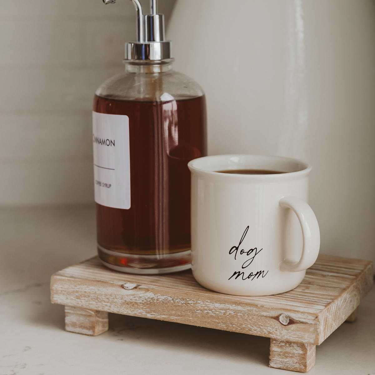 Impish Greetings 11 oz white ceramic campfire-style coffee mug with dog mom script text on a small wooden riser
