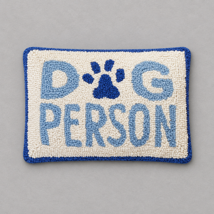 Impish Greetings Dog Person rectangular hook pillow with cream wool front, blue text, and a blue paw print design.