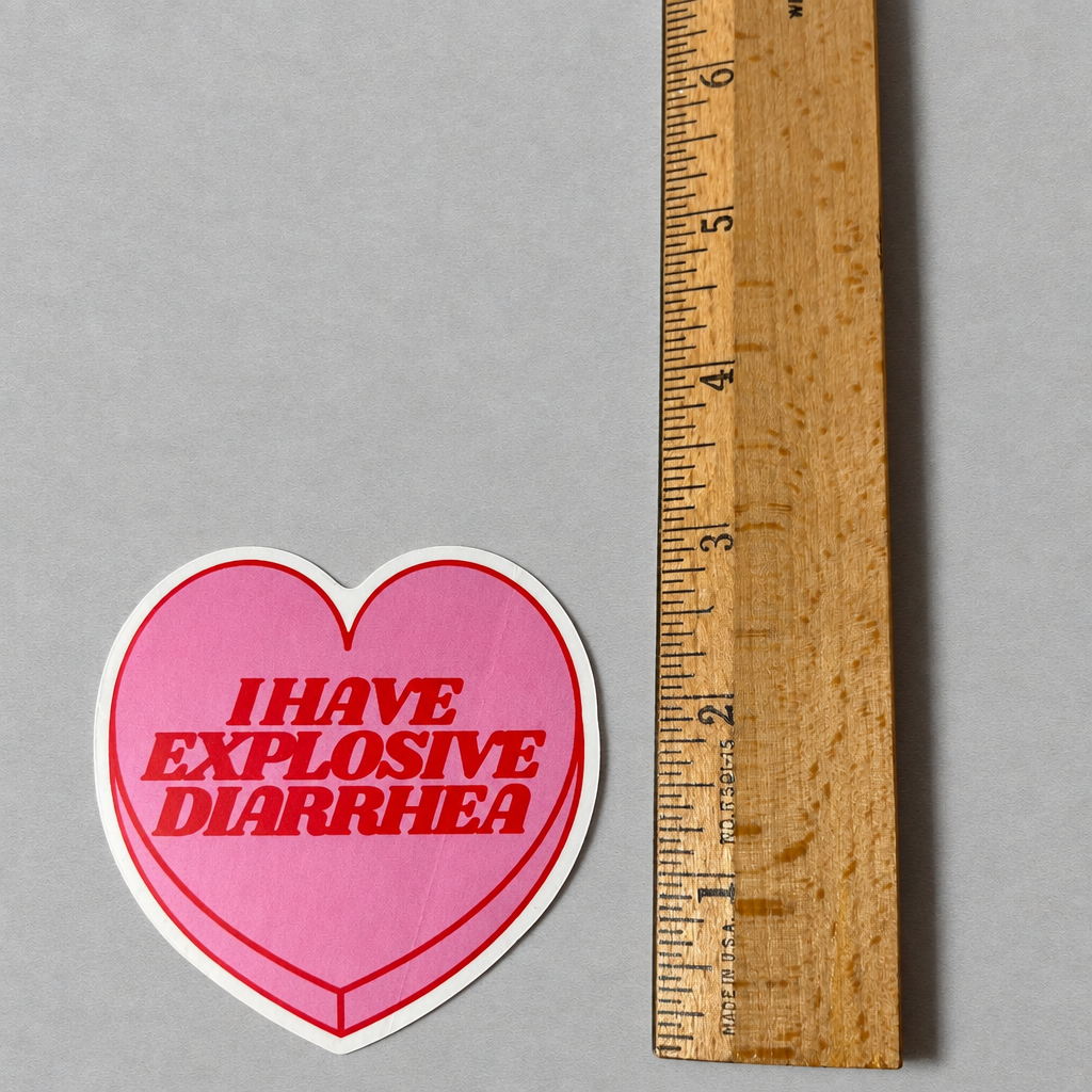 Impish Greetings heart-shaped pink vinyl sticker with red text reading I HAVE EXPLOSIVE DIARRHEA next to a ruler.