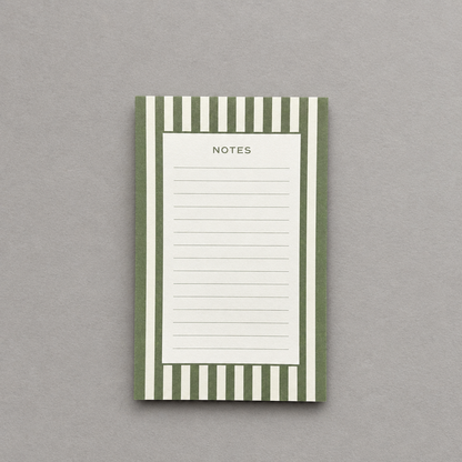 Impish Greetings green and white striped notepad with lined pages for notes on a neutral grey background.