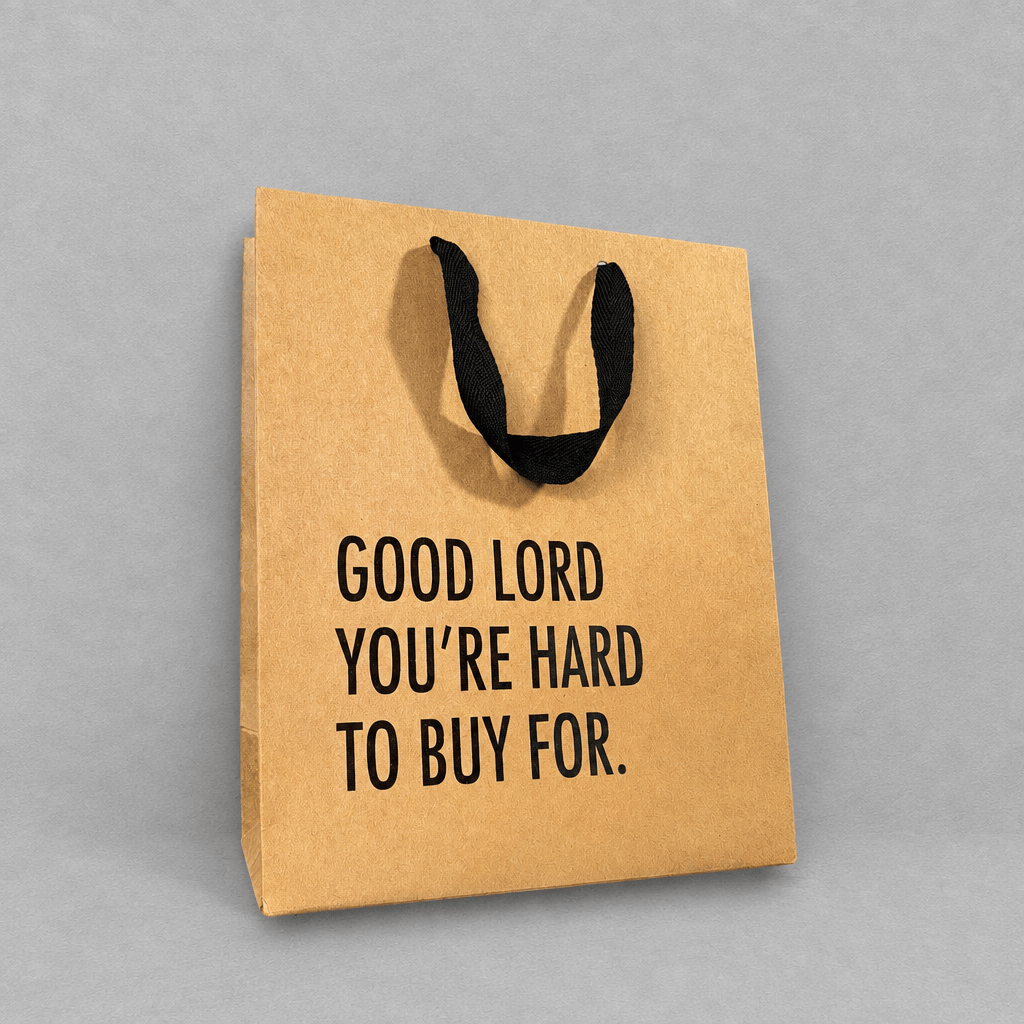 Impish Greetings kraft paper gift bag with black cloth handles and the text Good Lord You're Hard To Buy For.