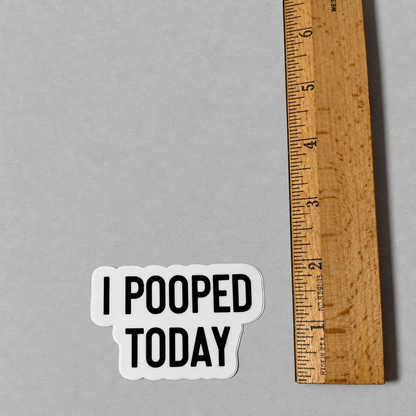 Impish Greetings I Pooped Today vinyl sticker with black text on a white background next to a wooden ruler