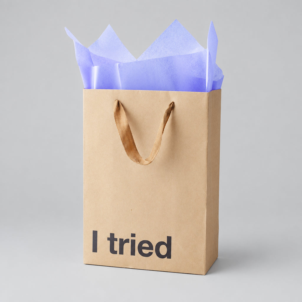 Impish Greetings kraft paper gift bag with I tried text and purple tissue paper on a light grey background
