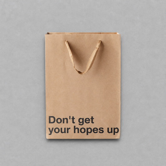 Impish Greetings kraft paper gift bag with black text reading Don't get your hopes up and brown ribbon handles.
