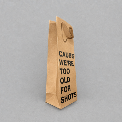 Impish Greetings kraft paper wine gift bag with black text reading Cause We're Too Old For Shots