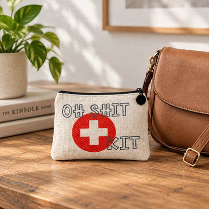Impish Greetings linen mini zipper bag with Oh Shit Kit text and red cross icon on a wooden table