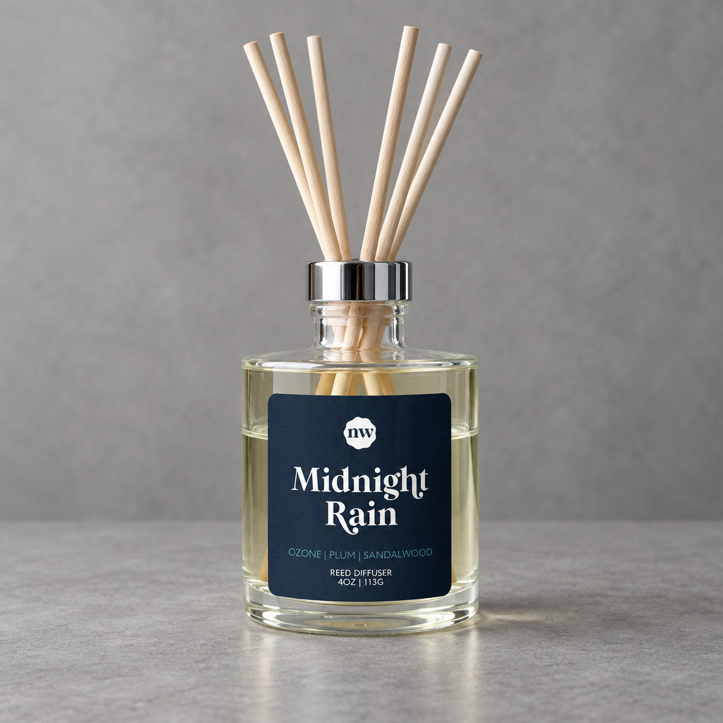 Impish Greetings Midnight Rain reed diffuser in a clear glass bottle with wooden reeds against a grey background
