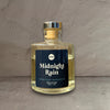 Impish Greetings Midnight Rain reed diffuser in a clear glass bottle with a dark blue label on a textured surface.
