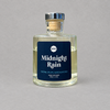Impish Greetings Midnight Rain reed diffuser in a clear glass bottle with a dark blue label on a grey background.