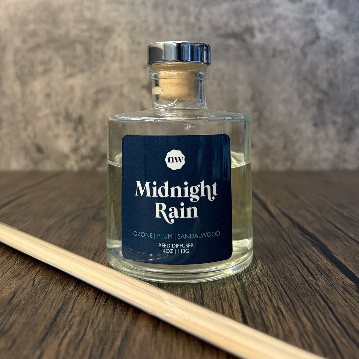 Impish Greetings Midnight Rain reed diffuser in a clear glass bottle with a dark blue label on a wooden surface.