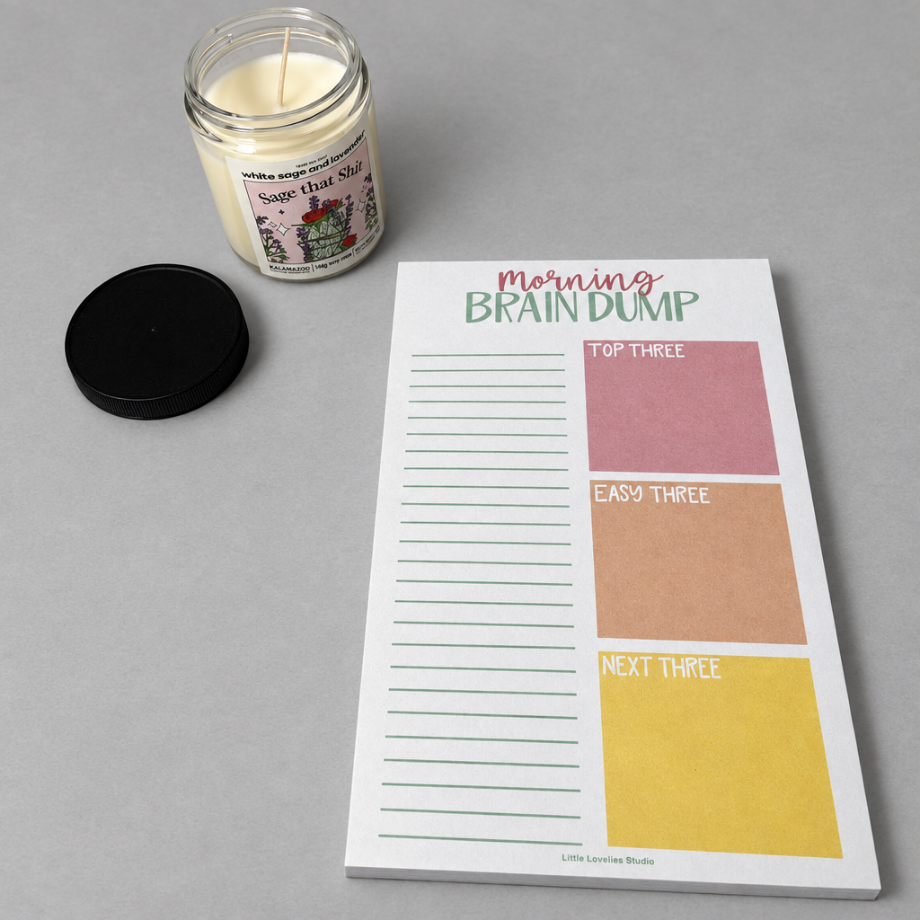 Impish Greetings Morning Brain Dump notepad with colorful task boxes and a scented candle on a grey surface.
