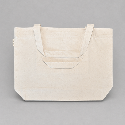 Impish Greetings natural cotton canvas tote bag with sturdy handles and side logo tab against a grey background