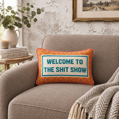 Impish Greetings needlepoint throw pillow with Welcome To The Shit Show text on a grey armchair