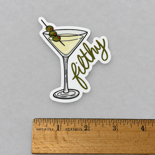Impish Greetings Filthy Dirty Olive Martini sticker featuring a cocktail glass with three olives on a wooden ruler.
