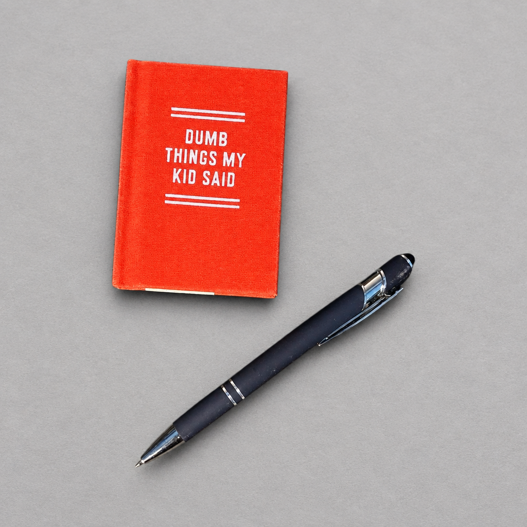 Impish Greetings Dumb Things My Kid Said tiny diary with a red felt hard-bound cover and gold-edged pages next to a pen