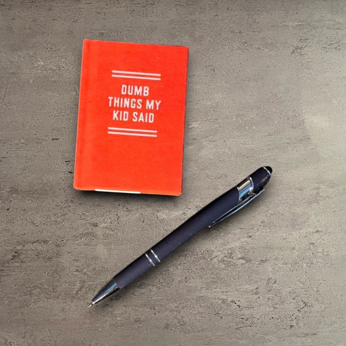 Impish Greetings Dumb Things My Kid Said tiny orange felt-covered journal with gold-edged pages and a black pen