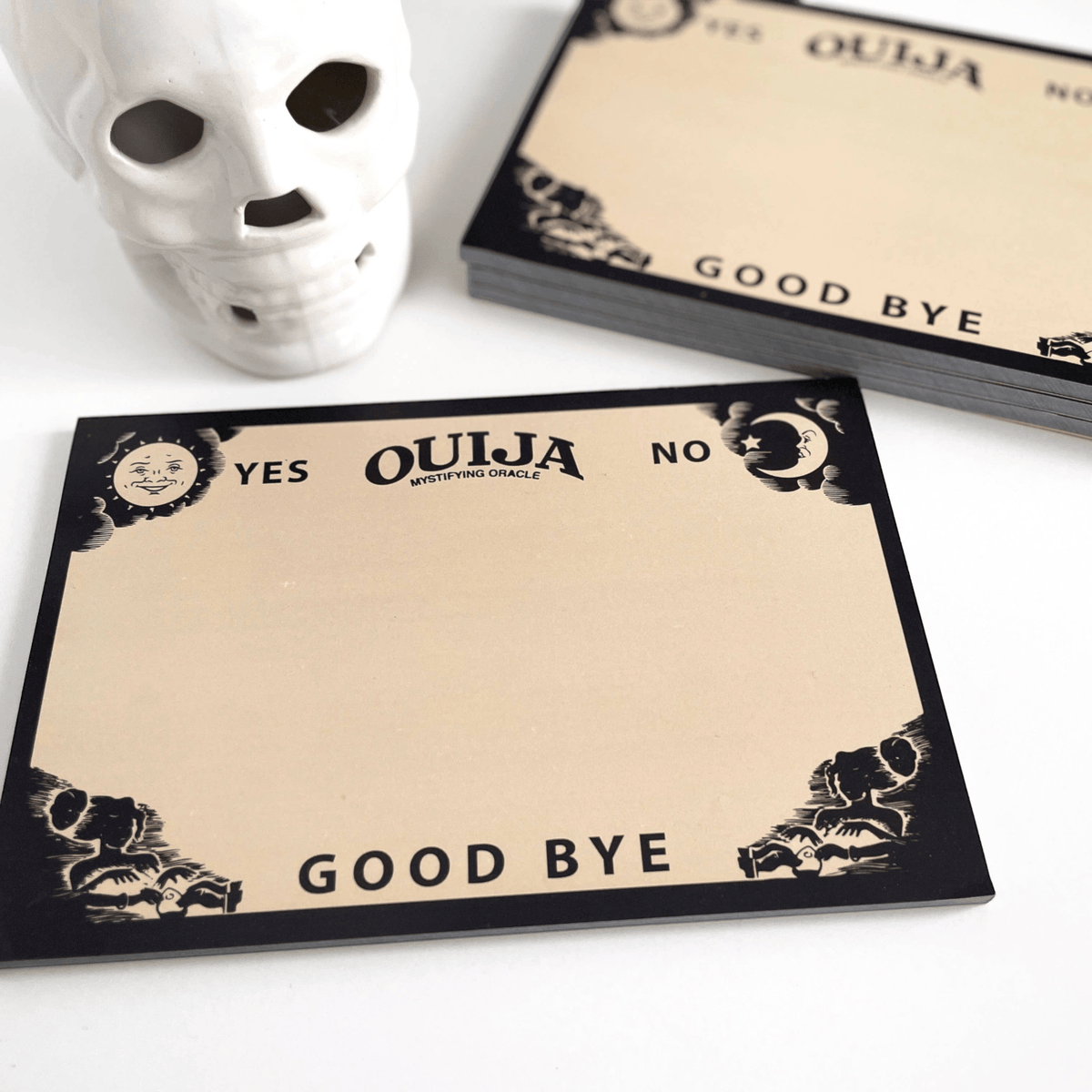 Impish Greetings Ouija board notepad with vintage spirit board design on recycled paper next to a white skull decor