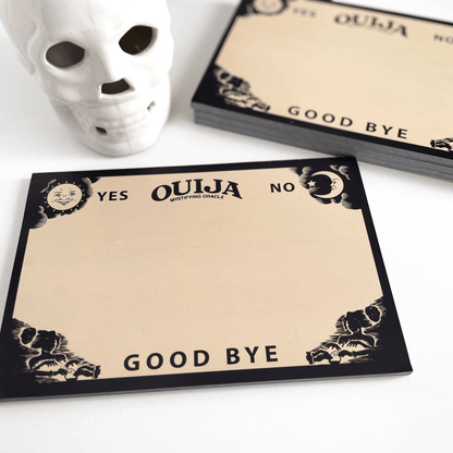 Impish Greetings Ouija board notepad with vintage spirit board design on recycled paper next to a white skull decor