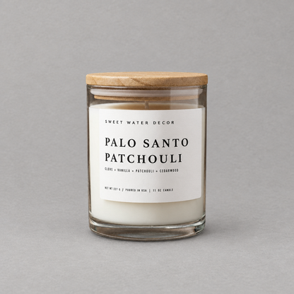 Impish Greetings Palo Santo Patchouli scented candle in a glass jar with a wooden lid on a grey background.