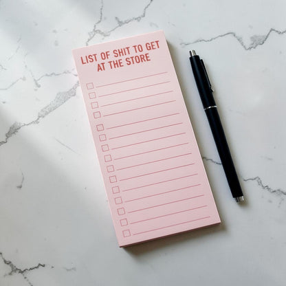 Impish Greetings magnetic shopping notepad in light pink with lined checklist and black pen on a marble surface.