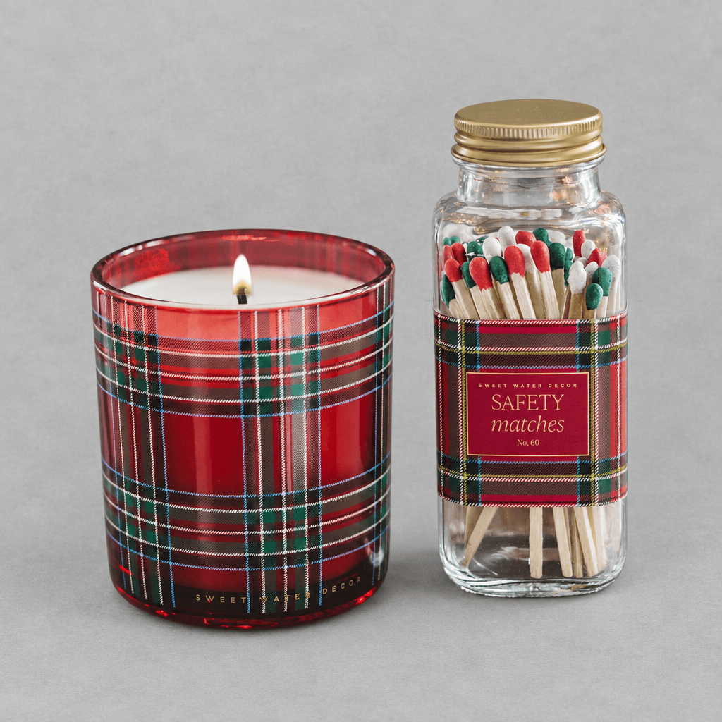 Impish Greetings soy candle in a red plaid glass jar next to a matching glass bottle of holiday safety matches
